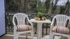 Deux chaises blanches avec des coussins à rayures sur un balcon, avec une table, une plante en pot et des fleurs oranges.