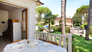 Un comedor con una mesa preparada para cuatro, mobiliario de exterior y vistas a un jardín cuidado y casas vecinas.