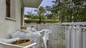 A balcony with a table set for two, white chairs, a woven basket, and a potted plant. - Villa Rosanna by Interhome (Lignano Pineta)