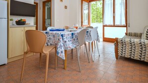 A dining area with a table set for four, a kitchen with a TV and fruit bowl, and a patterned sofa. - Villa Rosanna by Interhome (Lignano Pineta)