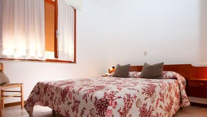 Ein Schlafzimmer mit einem Bett, einem Sessel, einem Nachttisch und einem Fenster mit Vorhängen.