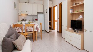Ein kompakter Wohnraum mit Küchenzeile, Essbereich, Fernseher und einem kleinen Bücherregal.