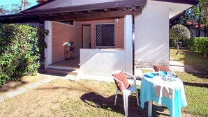 Ein kleines Backsteinhaus mit einer Veranda, einem Tisch mit Stühlen und einem Garten.