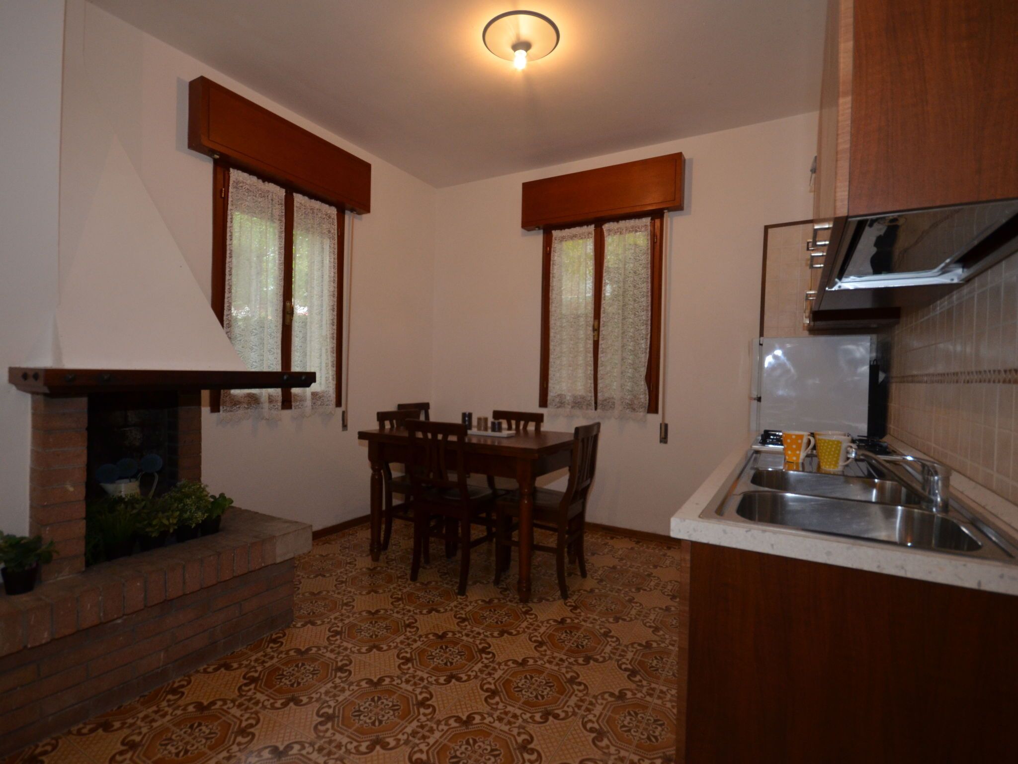 Una cocina compacta con una mesa de comedor, dos ventanas con cortinas, una estufa integrada y un salpicadero de azulejos.