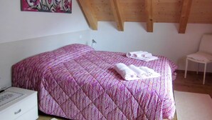 Een slaapkamer met een bed, een stoel, een witte dressoir en een schilderij aan de muur.