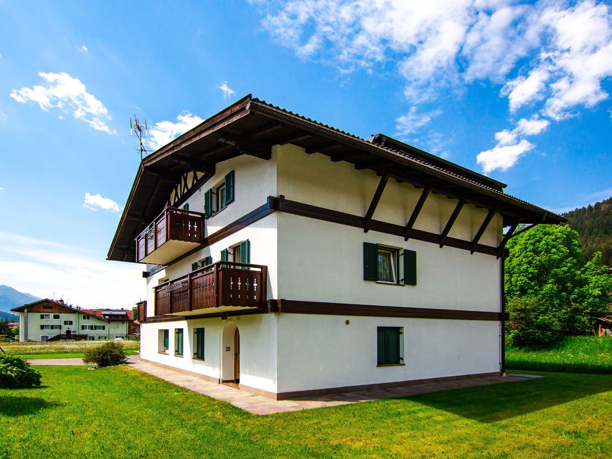 Ein zweistöckiges Gebäude mit Balkon, flachem Dach und einem kleinen Garten vor der Fassade.