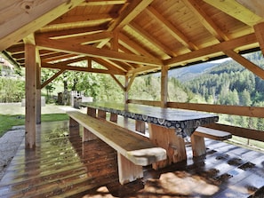 A wooden picnic table with benches under a covered area with a view of a forested mountain range.