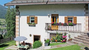 Een gebouw met twee verdiepingen, een balkon, een eethoek met parasol en een tuin met bloempotten.