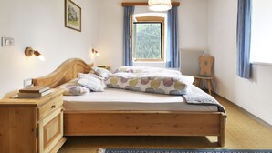 Een houten bed met hoofdeinde, nachtkastjes, een nachtkast en een radiator, plus een raam met gordijnen.