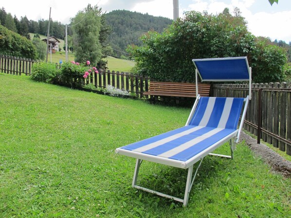 Een blauw-witte gestreepte lounge stoel in een grasveld, met een houten hek en een houten bankje op de achtergrond.