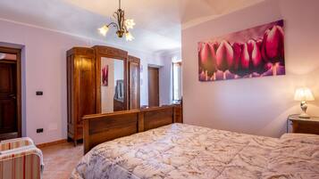 Une chambre à coucher avec un grand lit, une armoire en bois, un miroir et un tableau représentant des fleurs accroché au mur.