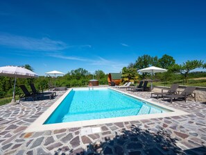 Una piscina con sillas de descanso y sombrillas, rodeada de baldosas de piedra y vegetación.
