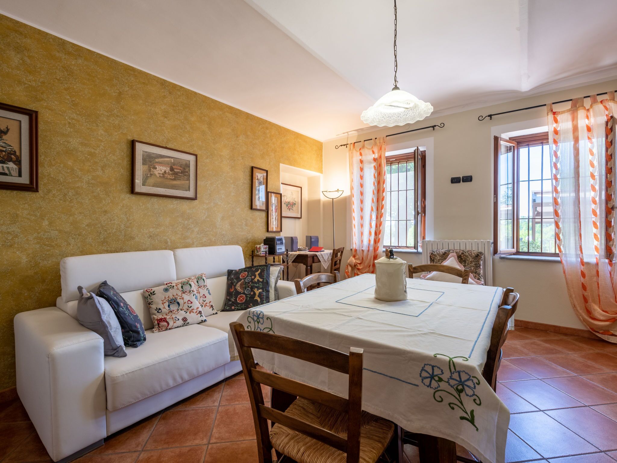 Un comedor con una mesa blanca para cuatro personas, un sofá blanco con cojines estampados, y una pared con cuadros enmarcados.