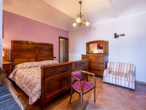 Un dormitorio con una cama y un aparador de madera, una silla, un sofá a rayas y una araña.