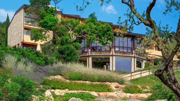 A modern building with a stone facade, a balcony, and a landscaped garden with rocks and shrubs. - Poiano Resort Appartamenti by Interhome (Garda)