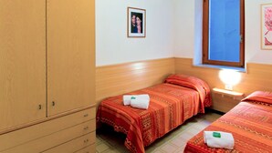 A hotel room with two beds, a wooden wardrobe, a small bedside table with a lamp, and a framed photo on the wall. - Apartment Gianni by Interhome (Torri del Benaco)