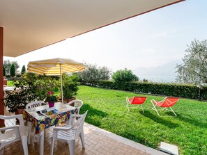 Une terrasse avec une table et des chaises, un parasol à rayures et une vue sur une pelouse verdoyante et des arbres.