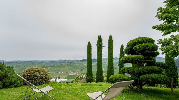 Two lawn chairs on a grassy hill overlooking a scenic landscape with rolling hills and a distant village.
