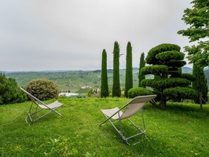 Dos sillas de jardín en una colina cubierta de hierba con vistas a un paisaje pintoresco de colinas onduladas y un pueblo lejano.