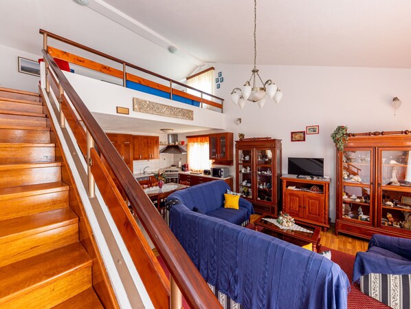 A spacious living area with a wooden staircase, a blue sofa set, a dining table, and a kitchen in the background. - Villa Saba by Interhome (Trogir)