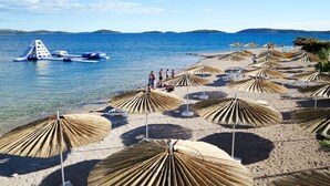 A beach with clear blue water, a small boat, and straw umbrellas. - Apartment Toni by Interhome (Šibenik)