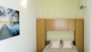 A bedroom with a wooden wardrobe, a bed with patterned bedding, and a painting of a pier. - Apartment Toni by Interhome (Šibenik)