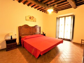 Un dormitorio con cama de madera, una mesita de noche, una lámpara, un cuadro en la pared y una ventana con vistas.
