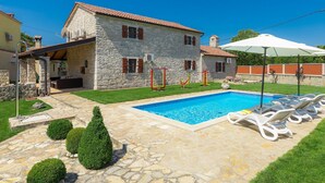Une maison en pierre avec une piscine, du mobilier d’extérieur et une pelouse bien entretenue.