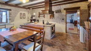 Une cuisine rustique avec des poutres apparentes, un mur en pierre et une table à manger en bois recouverte d’une nappe à carreaux.