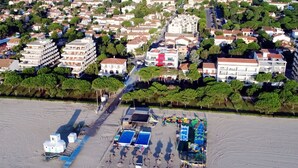 An aerial view of a coastal town with residential buildings, a sandy beach, and a small commercial area with umbrellas and beach chairs. - La Palangre by Interhome (Argelès sur Mer)
