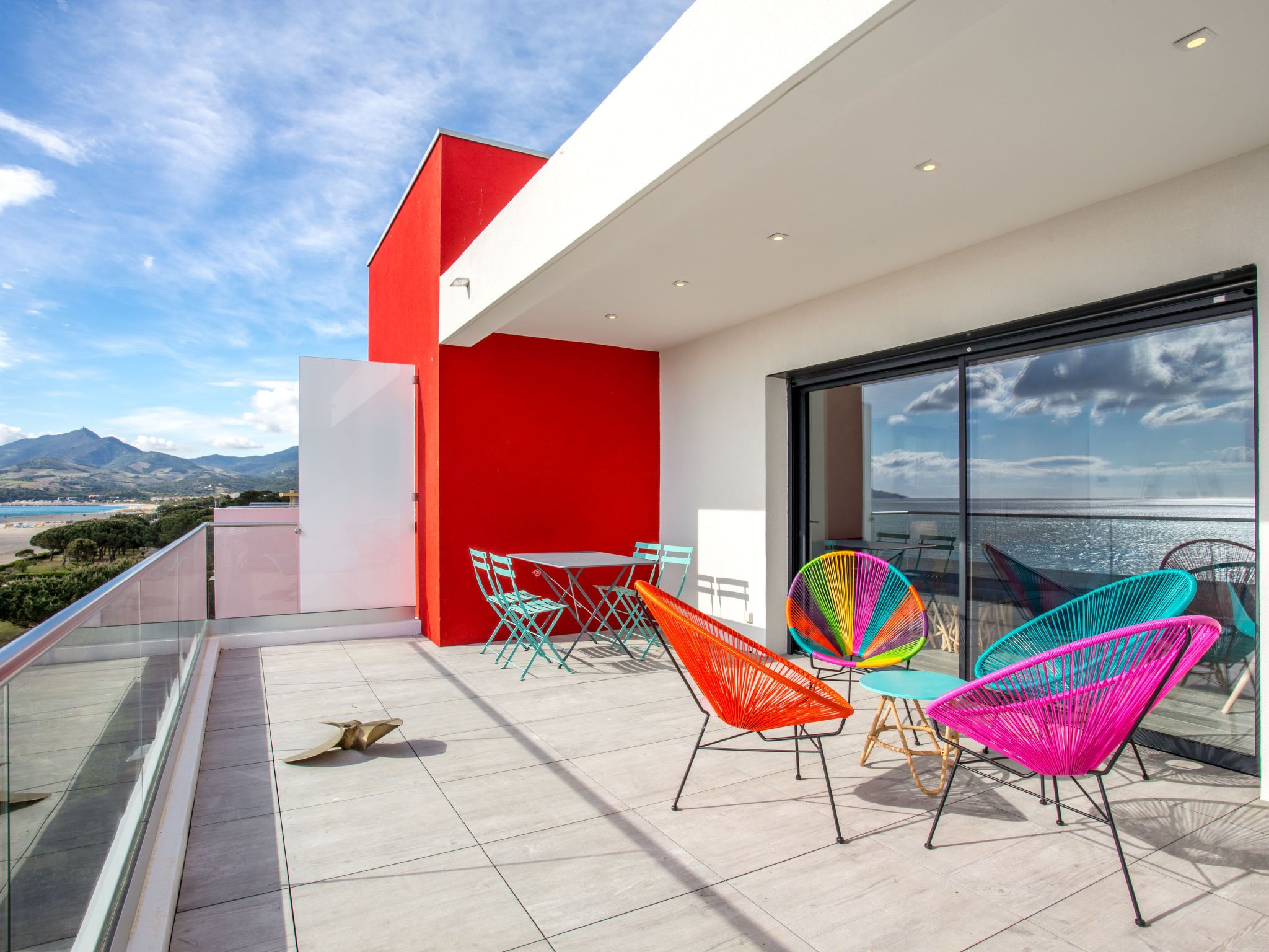 A modern balcony with colorful chairs and a glass railing overlooking a scenic landscape.