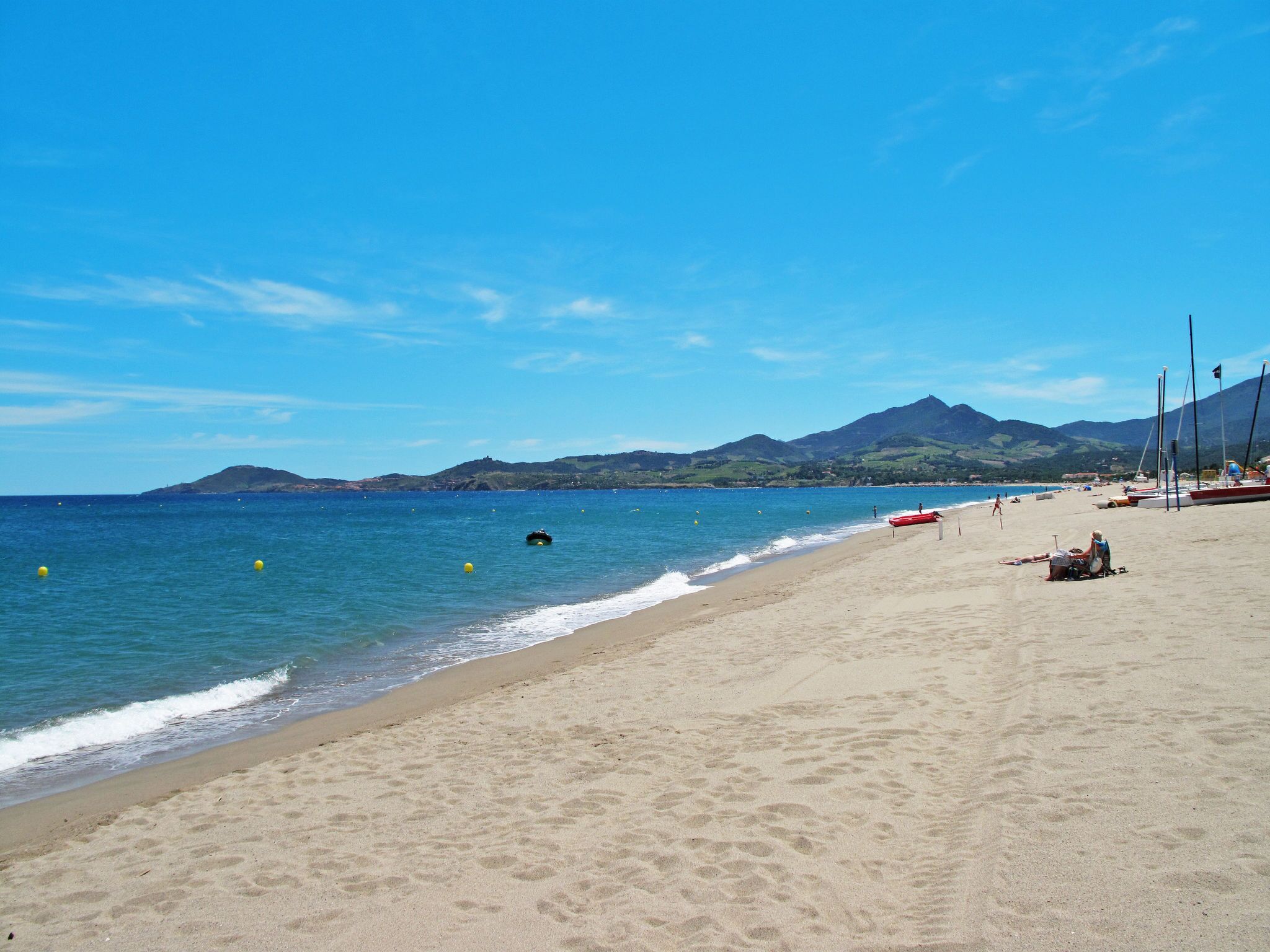 A beach with clear blue water, sandy shore, and distant mountains.