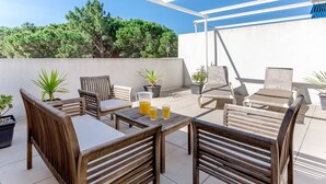 Ein möblierter Patio-Bereich im Freien mit Holzmöbeln, darunter Stühle und ein Tisch, und Topfpflanzen.