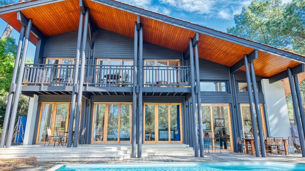 Una casa moderna de dos pisos con un balcón grande, una piscina y una terraza de madera.