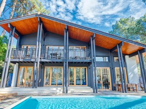 Una casa moderna de dos pisos con un balcón grande, una piscina y una terraza de madera.