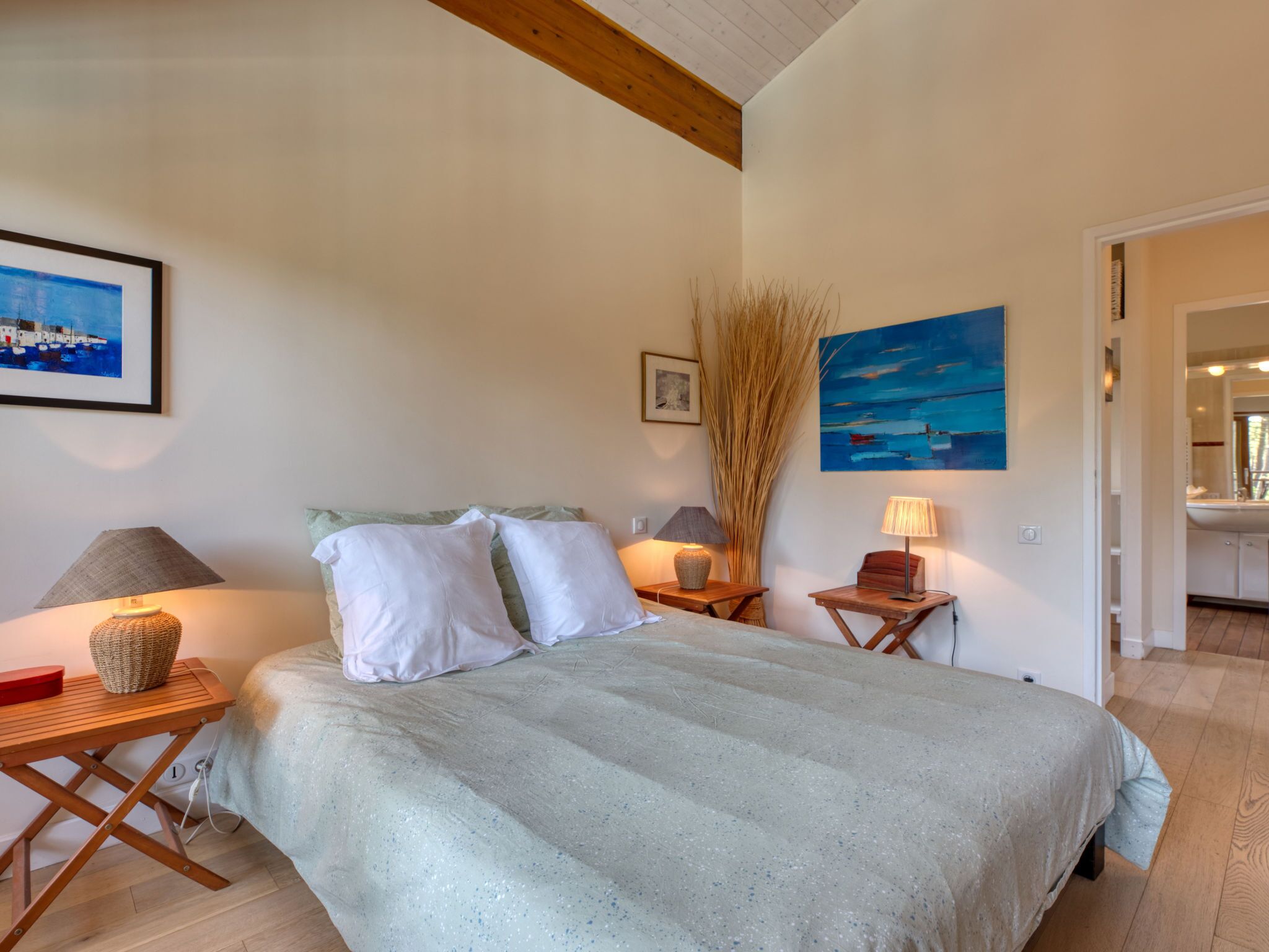 A bedroom with a bed, bedside tables, lamps, and artwork on the walls.