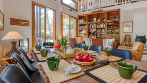 Un salón comedor amplio con techo alto, ventanas grandes, un balcón y una estantería bien surtida.