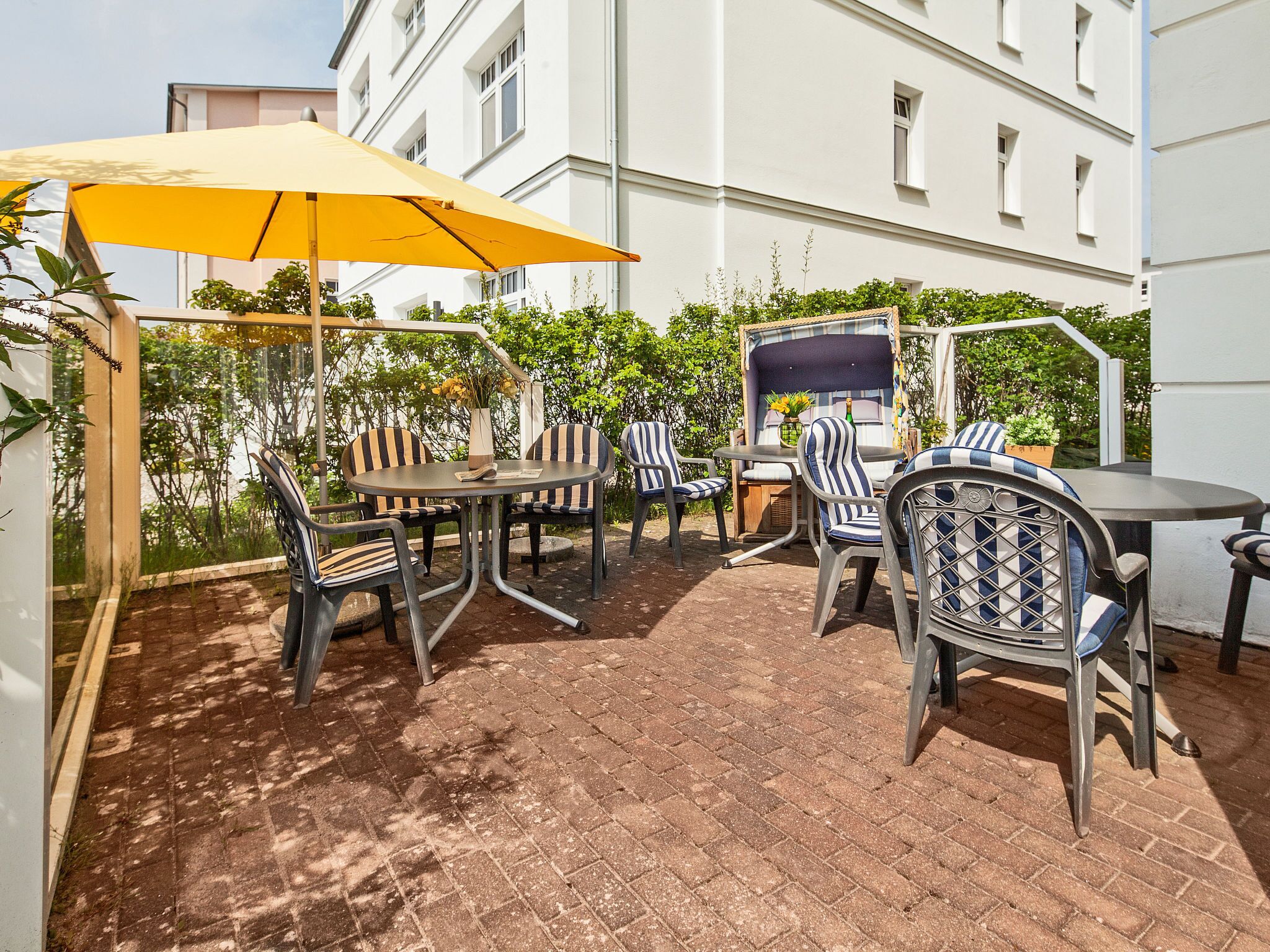 An outdoor patio with a yellow umbrella, metal chairs, and a table.