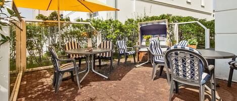 An outdoor patio with a yellow umbrella, metal chairs, and a table.
