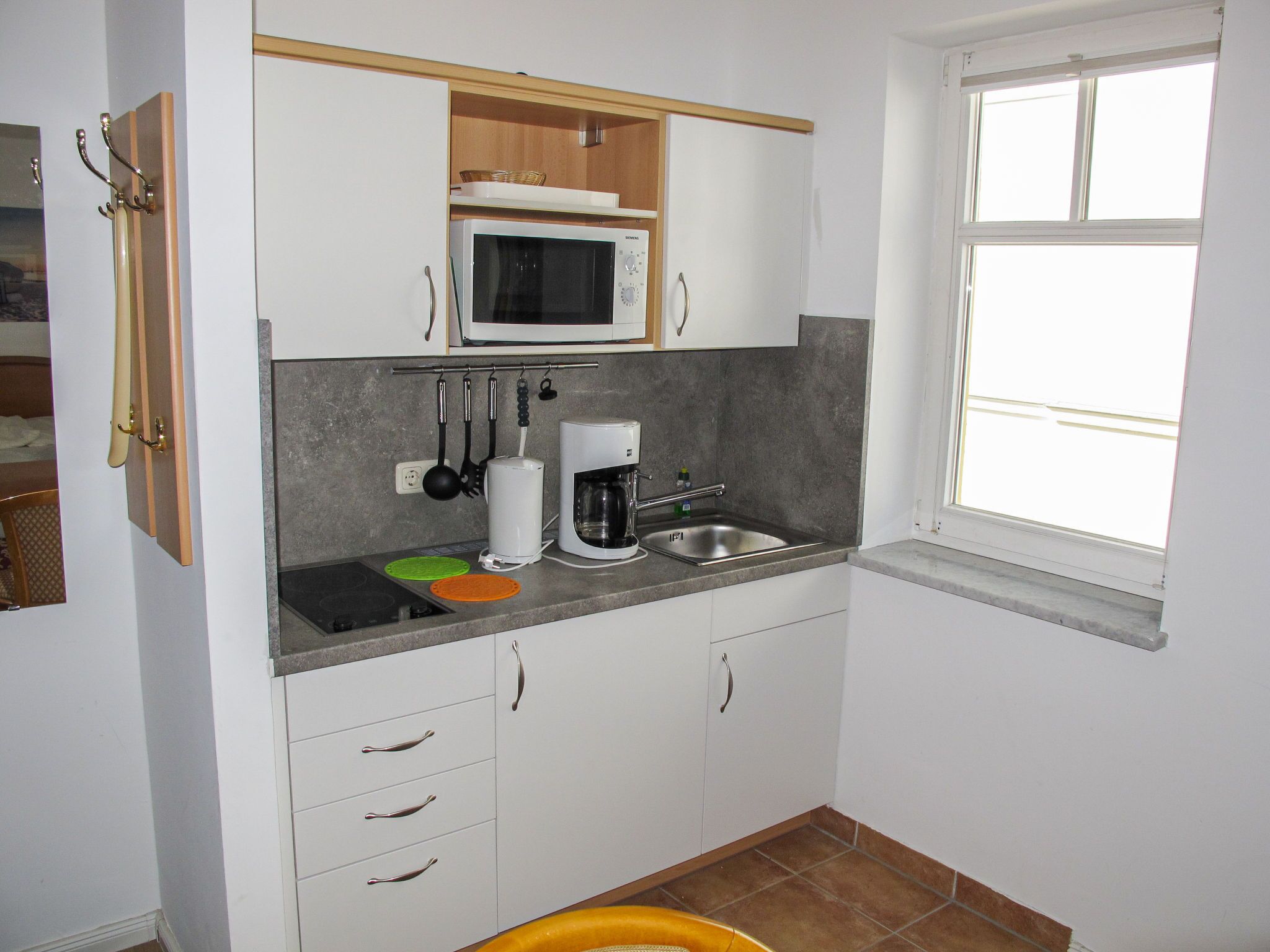 A compact kitchen with white cabinets, a microwave, a coffee maker, and a sink.