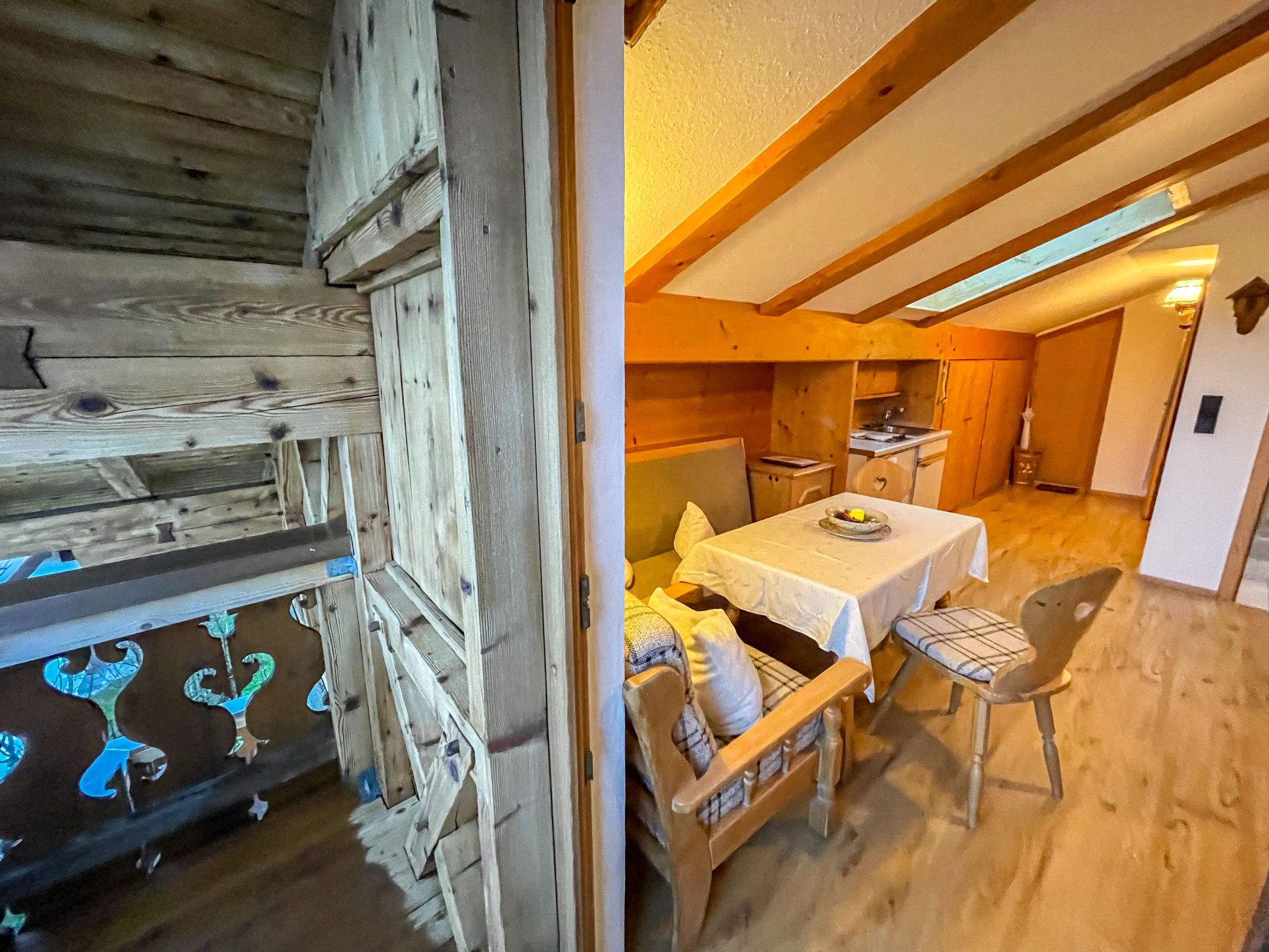 Ein rustikales Holzinterieur mit einem Essbereich, der einen Tisch und Stühle beinhaltet, einer Küche im Hintergrund und einer Holzbalkendecke.