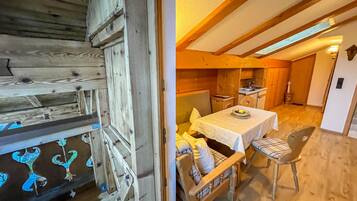 Ein rustikales Holzinterieur mit einem Essbereich, der einen Tisch und Stühle beinhaltet, einer Küche im Hintergrund und einer Holzbalkendecke.
