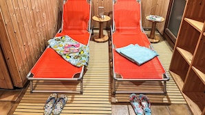 Two single beds with red mattresses and colorful blankets, a small table with a book, and a pair of flip-flops on the floor.