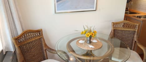 A dining area with wicker chairs, a glass table, and a framed painting on the wall.