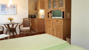 A cozy room with a bed, a dining table with chairs, a kitchen area with a microwave, and a cabinet with a television. - Landhaus Mahnhamm by Interhome (Horumersiel)