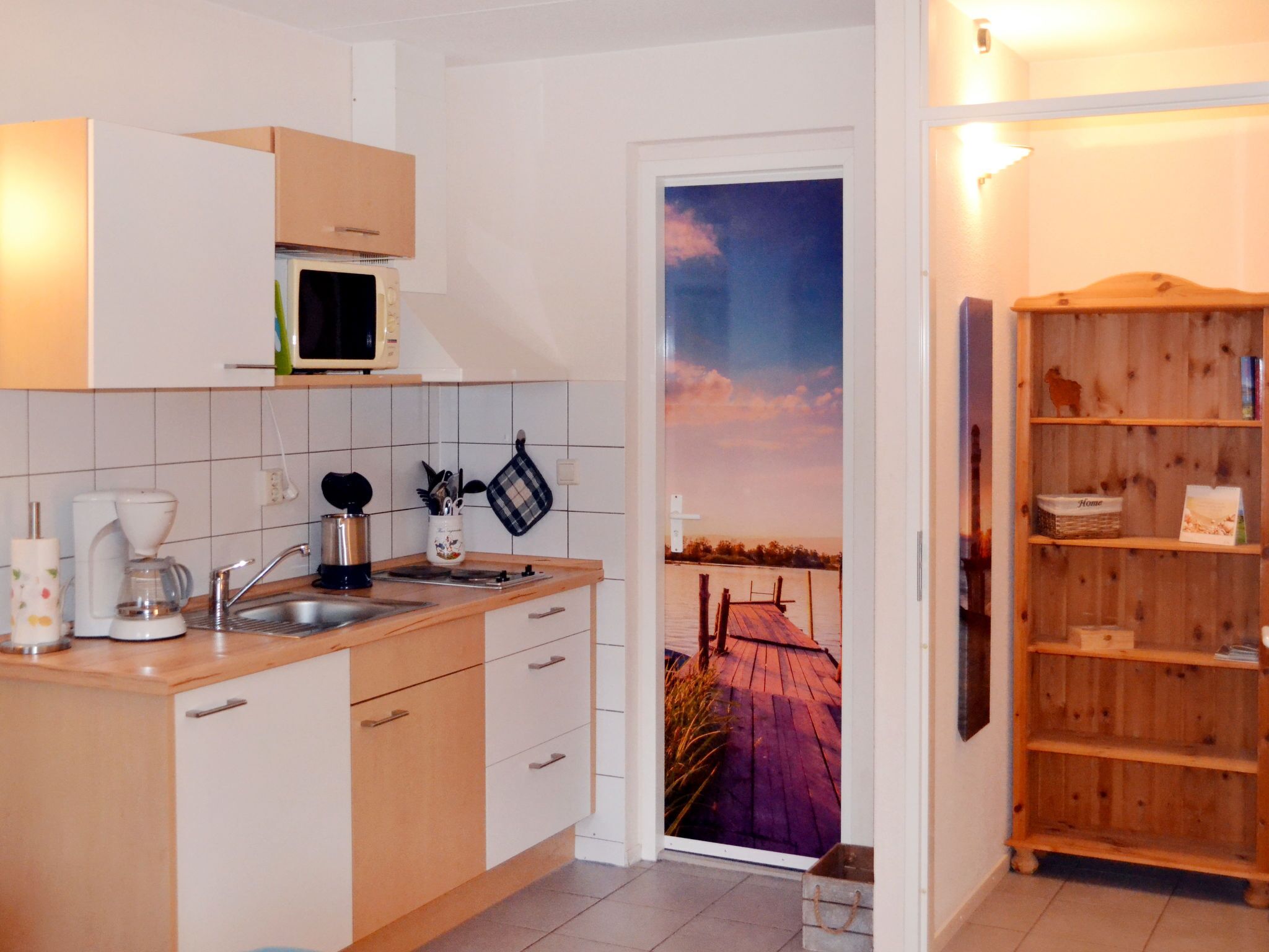A kitchen with a microwave, coffee maker, and utensils on the counter. There is a wooden shelf with items on it.