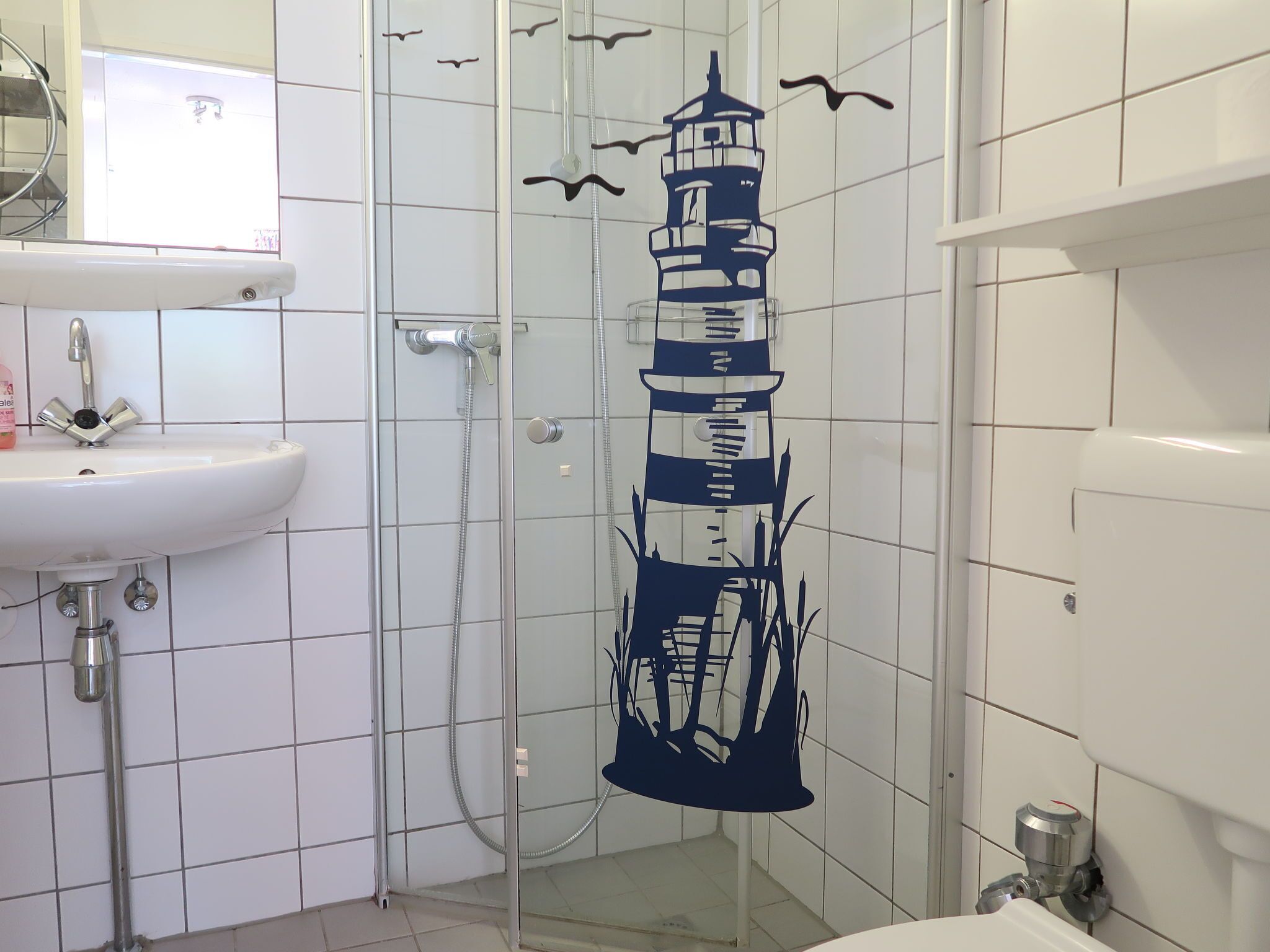 A bathroom with a white sink, a glass shower enclosure, and a decorative lighthouse mural.