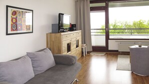A modern living room with a grey sofa, wooden cabinets, a television, and a view of greenery through large windows. - Ostsee-Residenz (DMP173) by Interhome (Damp)