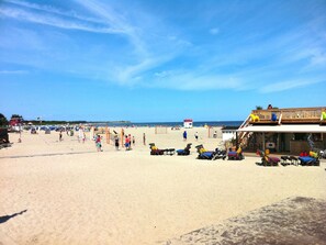 Una playa con tumbonas y sombrillas, una torre de salvavidas y un edificio con terraza de madera.
