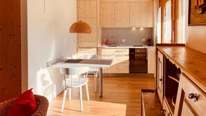 Una cocina moderna con armarios de madera, horno empotrado y comedor con mesa y sillas blancas.
